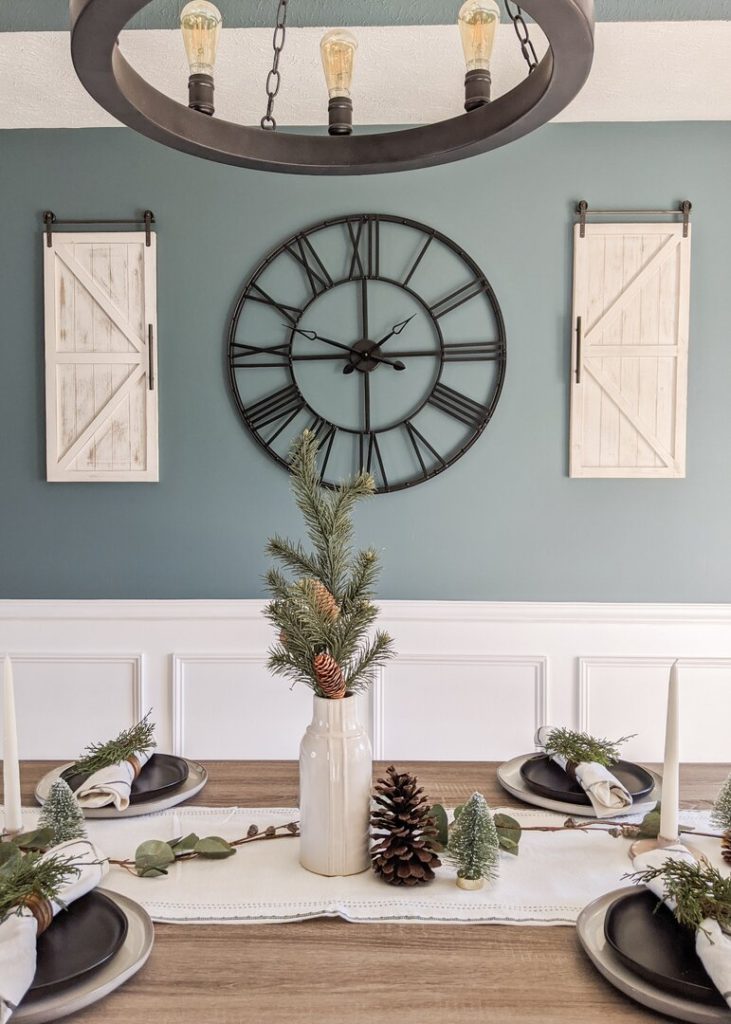 a dining room table decorated with plates, napkins, a vase, christmas trees, and pinecones