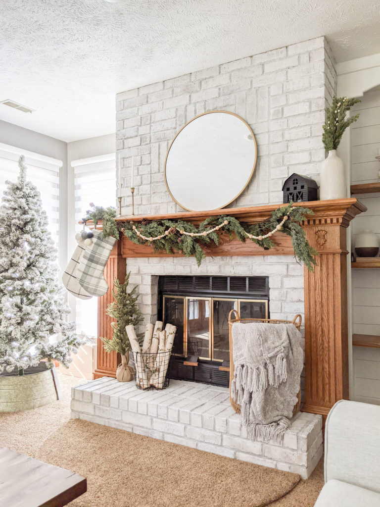 a christmas decorated fireplace mantle with garland, trees, stockings, and a basket