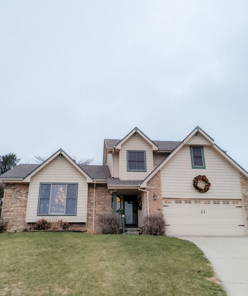 the exterior of a farmhouse home decorated for Christmas with a large wreath and a Christmas tree in the window